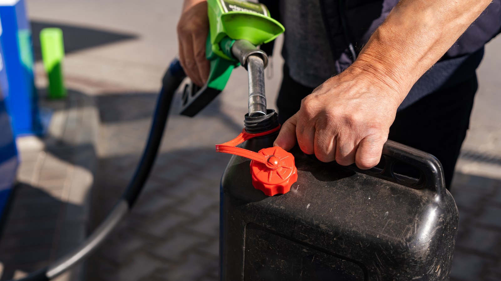 Une personne remplit un bidon de carburant a la pompe d'une station-service