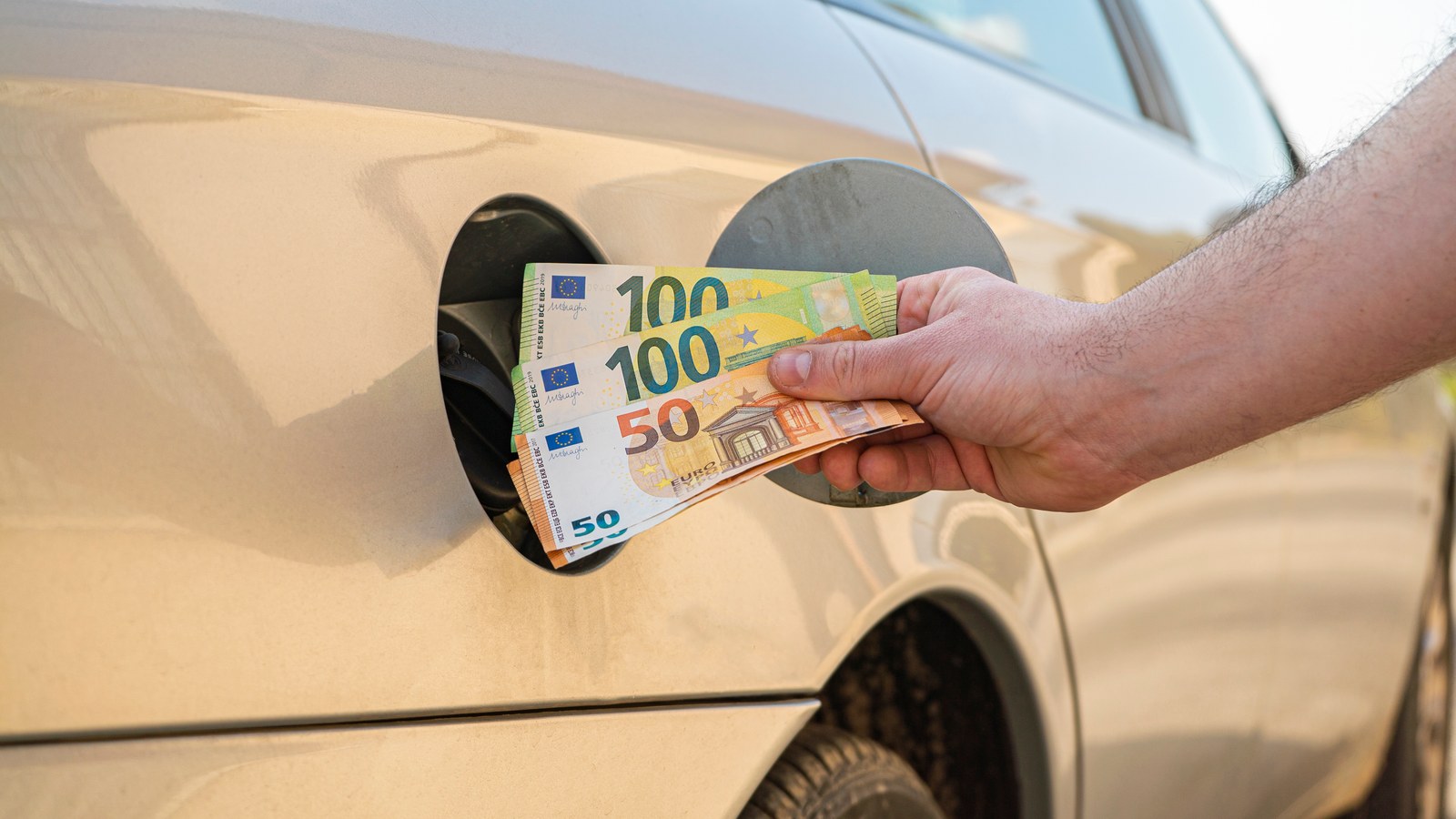 Main glissant des billets en euros dans la trappe à carburant d'une voiture